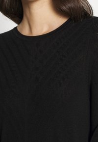 Schwarzer Pullover mit Rippstruktur und Zickzackmuster, rundem Halsausschnitt und weichem Material. Das Design ist minimalistisch und elegant.
