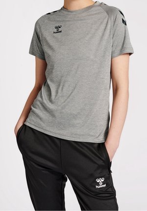 Person iført en grå hummel kortærmet trøje og sorte hummel træningsbukser med hænderne i lommerne mod hvid baggrund.