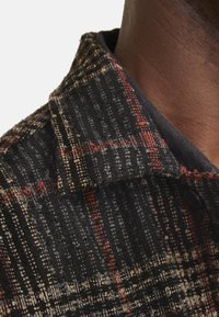 Gewebte Jacke in Schwarz, Rot und Creme mit einem strukturierten Muster. Sie verfügt über einen Kragen und Knopfdetails und zeigt ein strukturiertes Design.