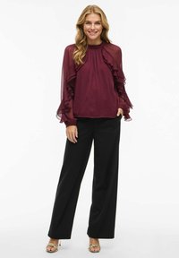 Bourgogne chiffonbluse med rynkede ærmer, parret med sorte vide bukser. Outfit kompletteret med stroppede gyldne sandaler.