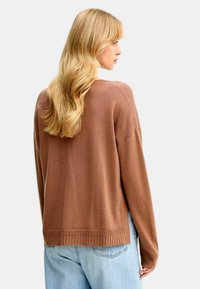 Maglione marrone a maglia con vestibilità rilassata, orlo a costine e spalle leggermente abbassate, abbinato a jeans azzurri chiari.