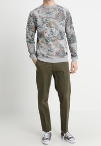 Sudadera gris con patrones florales en verde, amarillo y rosa; combinada con pantalones verde oliva y zapatillas grises con cordones blancos.