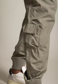 Cargo byxor i ljusgrått material med en sidoficka med lock, elastiska muddar och en avslappnad passform, matchade med vita sneakers.