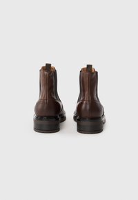 Bottines en cuir marron avec panneaux latéraux élastiques, une languette de traction et un talon empilé, présentant une texture lisse et un design épuré.
