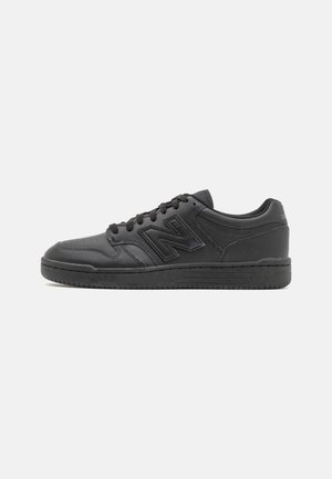 Sort lavtop sneaker med snørebånd, perforeret tå, polstret krave og et stort syet "N"-logo på siden.