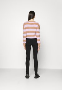 Suéter de rayas marrón difuso y lavanda con mangas largas, combinado con leggins negros y zapatos negros, visto desde la parte de atrás.