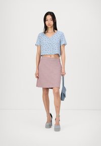 Top corto de manga corta en azul claro con patrón floral; combinado con una falda rosa hasta la rodilla. Zapatos de plataforma grises, sosteniendo un bolso azul.