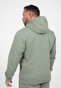 Groene hoodie met een zachte textuur, geribbelde manchetten en een buidelzak. De achterkant heeft een relaxed fit met een zichtbare capuchon.