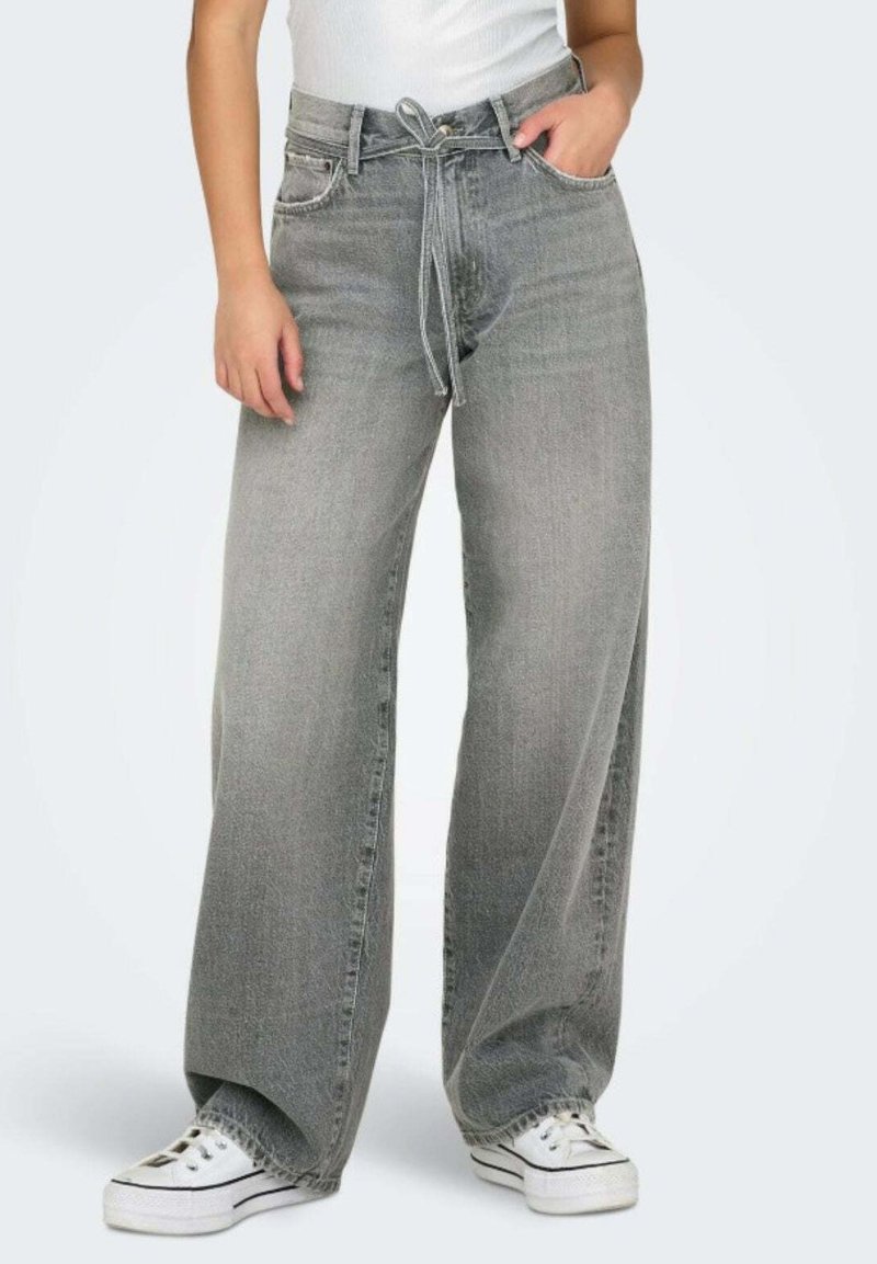 Jeans a gamba larga grigio chiaro in denim, con vita regolabile tramite cordoncino. Abbinati a sneakers bianche, i pantaloni hanno una vestibilità casual.