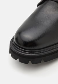 Zwarte leren laars met een ronde neus, voorzien van een dikke, gestructureerde zwarte rubberen zool en zichtbare stiksels langs de rand.