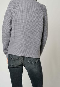 Pull en maille gris clair avec une surface texturée en relief, ourlet et poignets côtelés, assorti à un jean denim foncé avec des poches arrière.