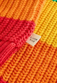 Tessuto a maglia multicolore con sezioni di un vivace arancione, rosso e giallo. Etichetta con la scritta "Little Bird" visibile vicino ai bordi.