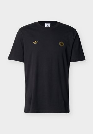 Camiseta negra de manga corta con logo dorado de Adidas en el lado izquierdo del pecho y un emblema circular dorado en el lado derecho del pecho.