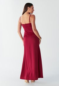 Ilga raudona satino vakarinė suknelė su plonomis petnešėlėmis, figūrą apgaubiančiu liemeniu ir lengvai krintančia sijonu. Nugaroje — diskretiška užtrauktuko dalis ir lygi tekstūra.