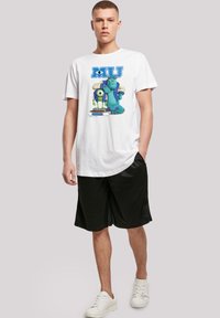 White cotton T-shirt featuring a graphic print of Monsters University characters. Paired with black shorts and white sneakers.
