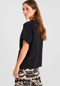 Top negro de manga corta hecho de una tela suave, con un corte holgado y cuello redondo, combinado con pantalones claros con patrones.