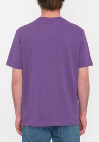 Camiseta corta de manga corta en color púrpura, fabricada en algodón suave con un diseño liso, que presenta un dobladillo recto y un cuello redondo.