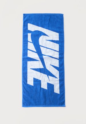 Serviette bleue avec grand texte blanc stylisé et motif swoosh, posée à plat sur un fond clair.