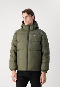 Olivgrüne Daunenjacke mit einem Reißverschluss vorne, elastischen Bündchen und einer Kapuze. Sie verfügt über horizontal gesteppten Abschnitte und ein kleines Logo-Patch.