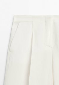 Pantalon blanc ajusté avec plis, poches latérales et une ceinture avec une fermeture avant cachée.