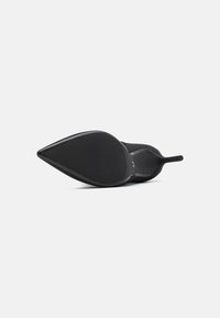 Zapato de tacón alto negro, con punta afilada, parte superior de tejido texturizado y suela de caucho lisa. Presenta un tacón delgado y un diseño minimalista.