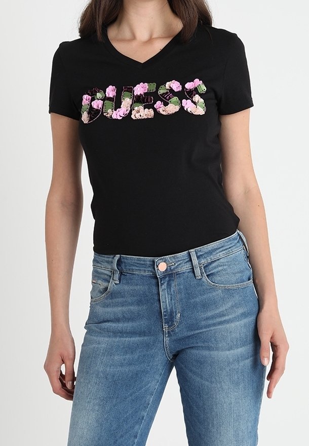 Musta v-pääntie t-paita, jossa on sana "GUESS" kukkakuosilla; yhdistetty sinisiin farkkuihin. Kangas on sileä ja siinä on slim fit -muotoilu.