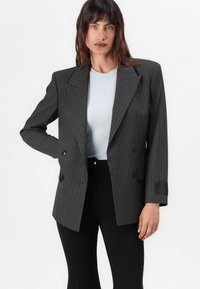 Blazer cu două rânduri de nasturi, din țesătură de pinstripe gri închis, cu reveruri croite, accente cu nasturi și o croială adaptată, asortat cu un top albastru.