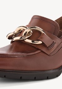 Mocassini in pelle marrone con una prominente catena dorata sulla parte anteriore, texture liscia e una robusta suola in gomma nera.