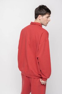 Piros pulóveres sweatshirt hajtottGallérral éslecsúszott válla, puha anyagból készült. Azonos színű piros nadrágra van húzva. Oldalnézet.