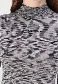 Dugi rukav, uska majica s visokim ovratnikom u sivoj i crnoj boji s teksturiranim uzorkom. Sadrži izvezeni logo "Karl Lagerfeld Jeans" na prsima.
