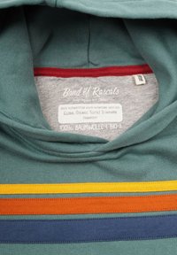 Vihreä puuvillaneule, jossa on moniväriset vaakaraitat keltaisena, oranssina, punaisena ja sinisenä. Tägissä lukee, että materiaali on 100% luomua.