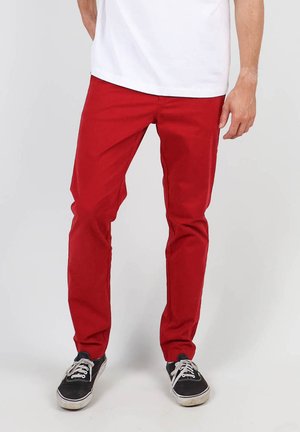 Pantalons en coton rouge mélangé avec une coupe droite. Portés avec un t-shirt blanc et des baskets noires, mettant en valeur une texture lisse et des lignes épurées.