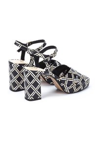 Sandalias de tacón alto en blanco y negro con un diseño de patrones, tacones gruesos, múltiples correas y material texturizado.