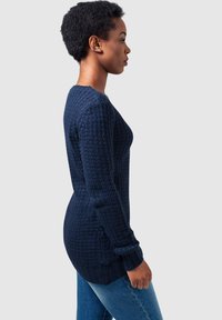 Maglione in maglia navy con un motivo testurizzato, polsini e orlo a costine, e una vestibilità leggermente allungata. Indossato con jeans blu.