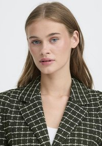 Zeleni in beli karirani blazer z izrezanim ovratnikom in teksturirano tkanino. Ima prilagojen kroj in zapiranje na en gumb.