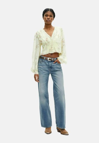 Blusa floreale gialla chiara, a maniche lunghe e tagliata; abbinata a jeans a gamba larga di un blu chiaro e stivaletti con tacco marroni. Dettaglio della cintura argentata.