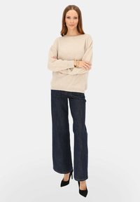 Beżowy, oversize'owy sweter z okrągłym dekoltem, zestawiony z szerokimi, granatowymi dżinsami i czarnymi szpilkami. Gładka faktura i luźny fason.