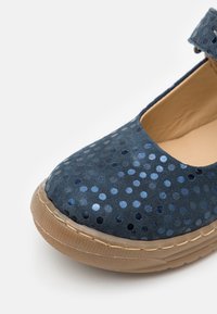 Niebieski zamszowy but z okrągłym, cekinowym wzorem, wyściełanym wnętrzem i gumową podeszwą. Posiada pasek na kostkę zapewniający pewne dopasowanie.