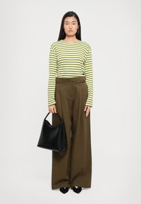 Green and white striped long-sleeve shirt; brown wide-leg trousers with a belt; holding a black leather handbag; black pointed-toe shoes.