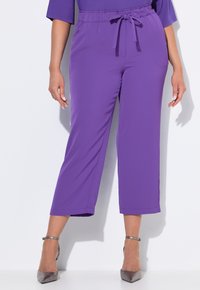 Pantalons violets taille haute avec cordon de serrage, design à jambes larges, texture lisse et longueur cropped, assortis à des chaussures à talons hauts métalliques.