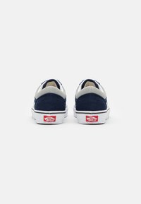 Baskets basses en nubuck bleu marine avec des accents gris et une semelle en caoutchouc blanche, arborant un logo rouge au niveau du talon et un design classique de col rembourré.