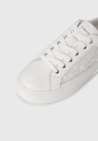 Valged sneakers, mille küljel on tekstuuriga detailid, laminaalne põhi ja sidumisseade. Tootemärk "PINKO" on nähtav küljel.