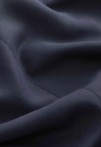 Tissu bleu marine foncé avec des coutures diagonales visibles et des plis doux mettant en valeur la texture et la douceur.