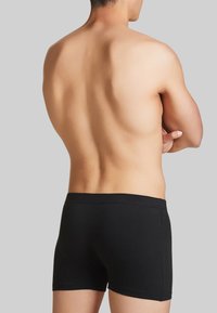 Boxer shorts neri in cotone con una texture liscia, caratterizzati da un design semplice e una fascia elastica in vita, mostrati su un torso nudo visto da dietro.