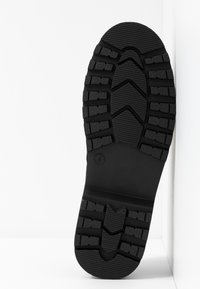 Semelle de chaussure en caoutchouc noir avec de profonds cannelures et motifs pour une traction optimale. Présente une section lisse près du talon et une surface texturée pour une meilleure adhérence.
