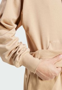 Sudadera beige con mangas largas gatherizadas y un bolsillo tipo canguro, hecha de una tela suave. Incluye puños y cintura de canalé.