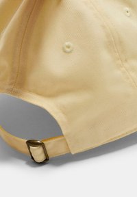 Helle gelbe Baumwollmütze mit gebogenem Schirm, strukturiertem Gewebe und einem Metallverschluss am verstellbaren Riemen auf der Rückseite.