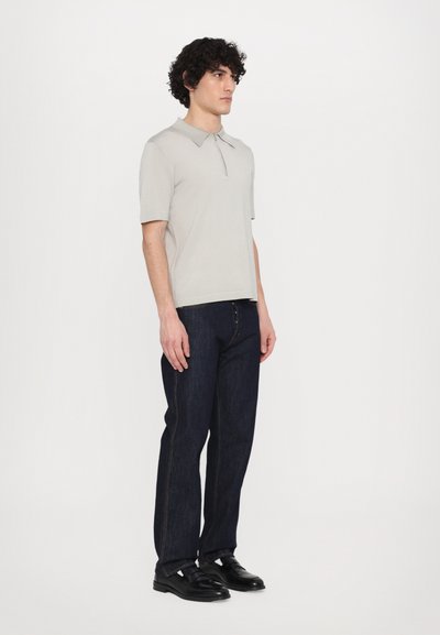 Polo grigio chiaro con colletto, abbinato a jeans in denim blu scuro. Tessuto liscio e design aderente, completato da scarpe nere.