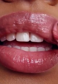 Couleur de lèvres rose glossy appliquée sur des lèvres pleines, mettant en valeur une texture lisse avec une brillance visible et des dents blanches en arrière-plan.
