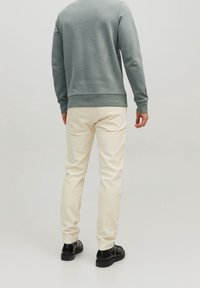 Lichtgrijze sweatshirt met ribbelmanchetten, gecombineerd met off-white jeans. De schoenen zijn zwart met een chunky zool. Beide kledingstukken hebben een eenvoudig ontwerp.